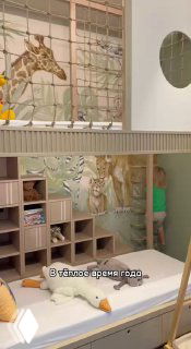 Игровая зона для ребёнка: мягкая кровать/мат с балансировочными подушками, стеллаж и роспись жирафа на стене.