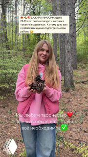 Женщина в розовой куртке в лесу держит шишки; фон — хвойный лес, сбор природных материалов для семейных поделок.