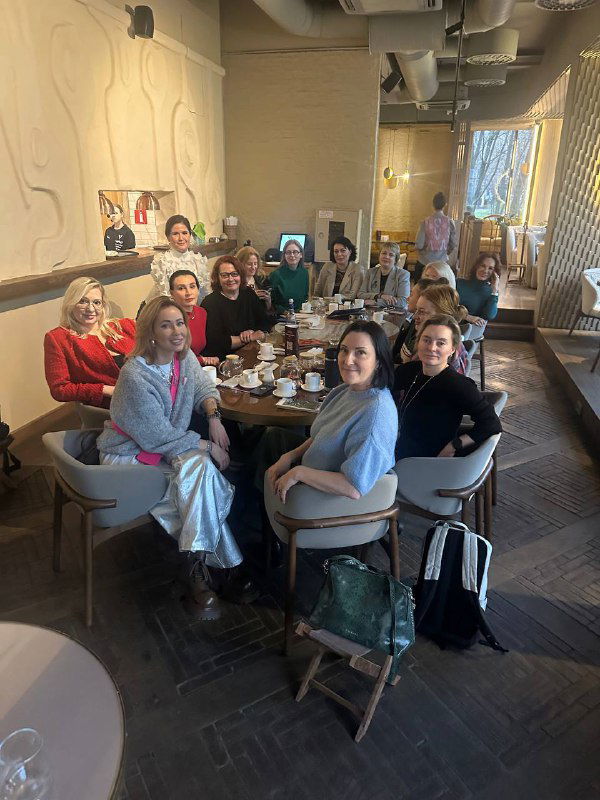 Групповая фотография в кафе: несколько женщин за большим общим столом, атмосфера нетворкинга и дружеского общения за чашками кофе.