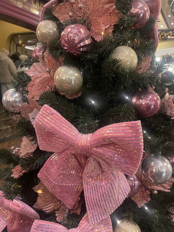 Крупный план рождественской игрушки и большой розовой банта на елочной ветке — праздничный декоративный элемент в торговой зоне.