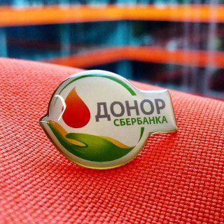 Значок с надписью «Донор» и логотипом Сбербанка на красной ткани, крупный план; иллюстрация темы «донорской» ипотеки.