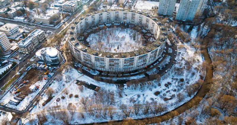 Аэровид с заснеженным домом-кольцом в Москве: круглая многоквартирная застройка, обступлённая дорогами и деревьями зимой.