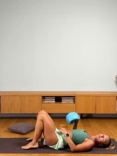 Инструктор лежит на коврике, показывает первое положение для работы с тазовым дном, в комнате видна подушка и минималистичный интерьер.