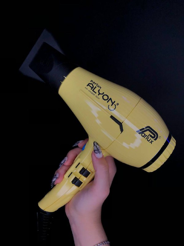 Жёлтый профессиональный фен в руке на чёрном фоне; видно маникюр владельца; фото товара для волос из магазина КРЕАТИВ в Калининграде.