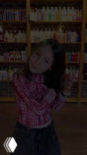 Девочка в салоне красоты с аккуратной стрижкой и лёгкой зелёной оконтовкой кончиков волос, стоит на фоне полок с косметикой.