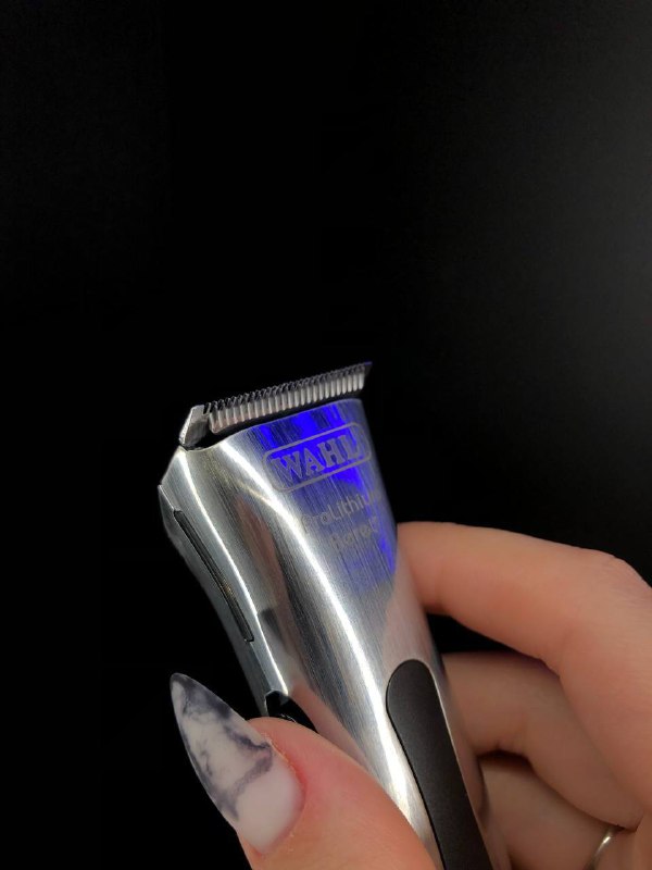 Профессиональная машинка для стрижки в руке на чёрном фоне; крупный план металлического корпуса и деталей, товар для салонов и парикмахеров.