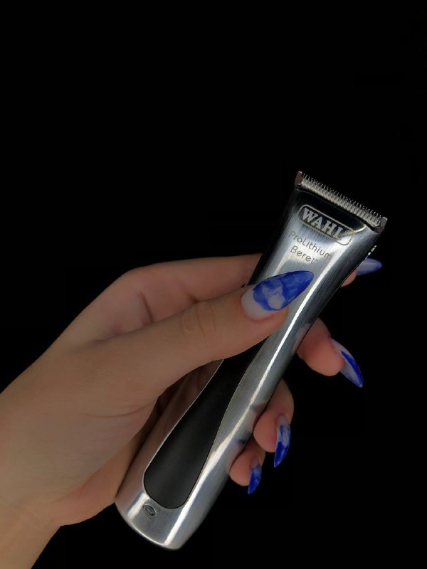 Триммер/машинка для стрижки в женской руке на тёмном фоне; видна рука с маникюром; демонстрация профессионального инструмента.