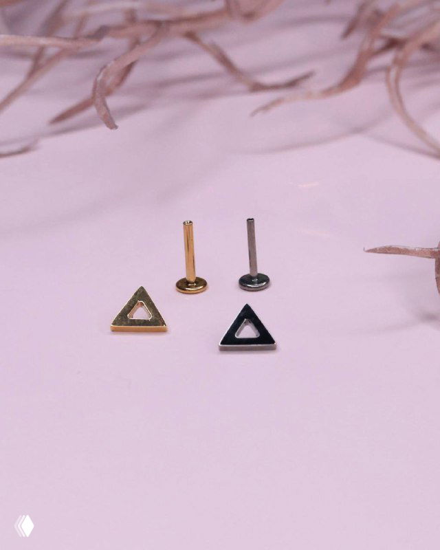 Титановый push-in и накрутки-треугольники на однотонном светло-розовом фоне: показаны золотистые и тёмные металлические элементы для пирсинга.
