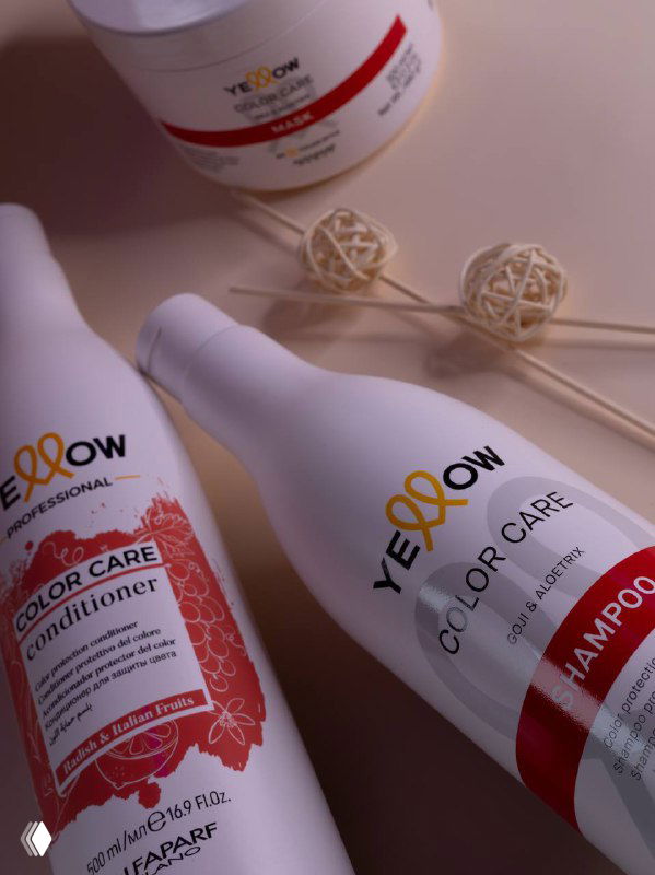 Крупный план белых флаконов и баночки Yellow Professional: продукты для ухода и окрашивания с красными этикетками на пастельном фоне.