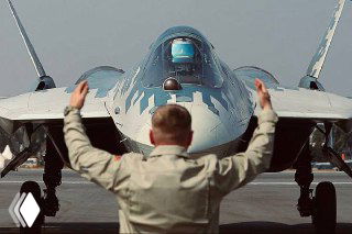 Наземный инженер руководит рулёжкой Су-57 на аэродроме, кадр показывает самолёт и специалиста на переднем плане в момент подготовки или сопровождения демонстрации.