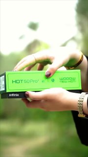 Крупный план: женские руки держат ярко‑зеленую коробку телефона с заметной надписью «HOT 50 Pro» и логотипом Infinix, размытый фон.