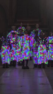 Фронтальный кадр коллектива моделей в разноцветных LED‑плащах: яркие пиксельные узоры покрывают поверхности одежды, эффектно смотрится на подиуме.