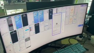Фото рабочего стола: изогнутый монитор с множеством открытых окон и вкладок интерфейсов, видна клавиатура и часть мыши.
