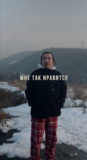 Превью: человек в тёмной куртке и клетчатых брюках стоит на заснеженной тропе на фоне холмов и неба.