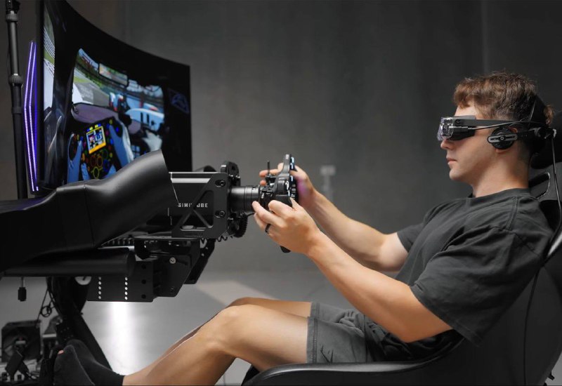 Человек в гоночном сиденье использует лёгкую VR-гарнитуру Bigscreen Beyond 2, держит руль симулятора; показана сцена использования устройства.