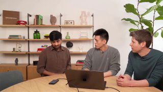 Три человека за столом в студии обсуждают демонстрацию: ноутбук, микрофон и оборудование на столе в дружеской рабочей обстановке.