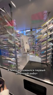 Вид через стеклянную витрину на аптеку с автоматическим аптечным роботом и рядами полок с лекарствами.