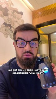 Мужчина в очках и с бородой показывает экран смартфона в комнате с настенной росписью; на фото видна подпись о ChatGPT