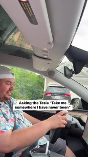 Мужчина в салоне электромобиля Tesla улыбается за рулём; видны приборная панель, сенсорный экран и открытое боковое окно.