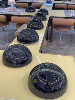 Интерьер ресторана с рядом куполообразных устройств или летающих тарелок, размещённых на длинном столе в зале, видны столы и стулья.