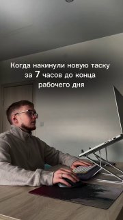 Мужчина за столом печатает на ноутбуке на подставке; минималистичное рабочее место, видна верхняя часть комнаты.