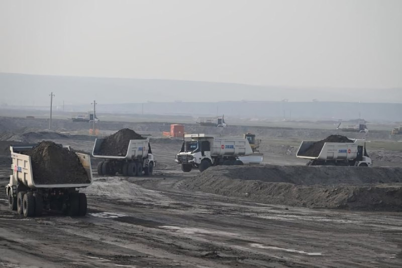 Несколько самосвалов движутся по грунтовой дороге карьера, видны разгрузочные участки, выемки и дальний горизонт добычного полигона.