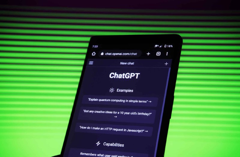 Смартфон крупным планом с открытым ChatGPT на экране, на фоне зелёных горизонтальных полос, тёмная студийная подсветка