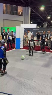 Группа гуманоидных роботов на демонстрационной площадке в выставочном зале, несколько посетителей наблюдают за показом и стендами, технологическая сцена.