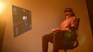 Силуэт человека в офисном кресле в VR-очках в тёплом освещении; на стене проекция игрового интерфейса, иллюстрация встроенного ПК в кресле.