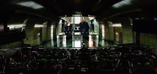Широкий панорамный вид иммерсивного показа с изогнутым экраном, на котором идёт финальная сцена, видны ряды просматривающих зрителей.