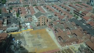 Аэрофотоснимок жилого квартала в Шанхае с видимыми рядами домов, пустой стройплощадкой и техникой внизу на фоне плотной застройки.