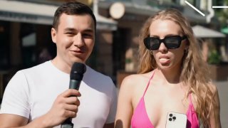 Мужчина с микрофоном берет уличное интервью у девушки в розовом купальнике с телефоном в руке на летней улице.