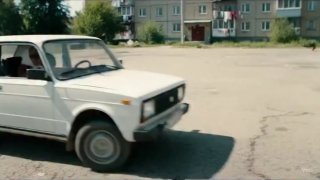 Фотография двора жилого дома: припаркованная белая легковая машина на асфальтовой площадке и пятиэтажные дома на заднем плане
