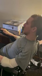 Мужчина в инвалидной коляске сидит у компьютера и играет в видеоигру; видно положение рук, мышь, кресло, бытовые предметы.