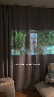 Проекция кадра фильма «Сумерки» на плотной шторе в комнате: крупный женский портрет на занавеси, виден диван и подушка.