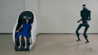Женщина в футуристическом кресле-пульте сидит в синем платье; рядом стоит черный человекоподобный робот, демонстрация работы системы.