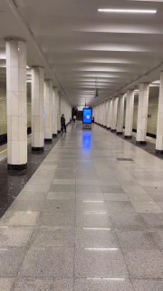 Пустая платформа московского метро с рядами колонн, освещённым потолком и плиточным полом; вдалеке виден светящийся экран.