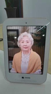 Фотография цифровой рамки с портретом пожилой женщины на экране; устройство стоит на столе, на заднем плане размытый интерьер