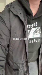 Крупный план торса человека в тёмной куртке и худи с графическим принтом; видна часть подбородка, подпись на фото и нейтральный фон.