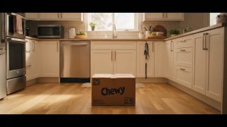 Картонная коробка с надписью Chewy стоит на полу светлой кухни; бытовая техника и естественный солнечный свет через окно формируют рекламный кадр.
