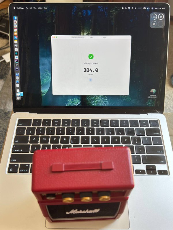 Фотография открытого MacBook: на экране видно приложение весов с цифровым значением, на клавиатуре лежит небольшой предмет, демонстрация измерения.