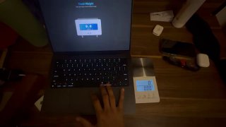 Сцена с MacBook и цифровыми кухонными весами рядом: на экране ноутбука приложение весов, рядом видна рука пользователя и показания внешних весов для сравнения.