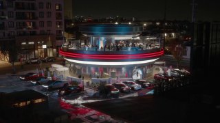 Ночная панорамная фотография ретро‑закусочной Tesla Diner в Голливуде: круглое двухэтажное здание с неоновой подсветкой и автомобилями на парковке.