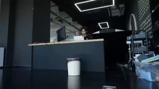 Кадр офисного пространства: на переднем плане небольшое автоматическое мусорное ведро, позади стол с компьютером и человек.