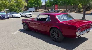 Красный классический Ford Mustang 1966 года на парковке, вид сзади-сбоку: показаны кузов, колёса и окружение улицы.