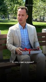 Мужчина в светлом пиджаке сидит на скамейке в парке и держит в руках коробку с предметом; кадр напоминает сцену из фильма.