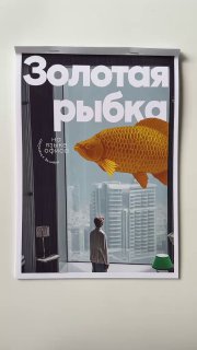 Постер с крупной золотой рыбкой на фоне городских высоток; человек в дверном проёме смотрит на неё, как на обложку.