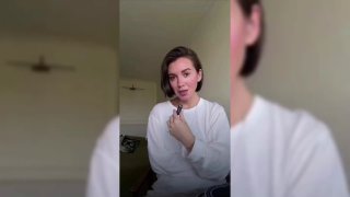 Вертикальное видео: человек в светлой одежде говорит в камеру в комнате; на фоне стена и мебель, фон слегка размытый