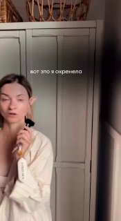 Кадр вертикального видео: человек держит кисть для макияжа на фоне платяного шкафа, видна домашняя обстановка и наложенный текст в ленте.