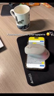 На столе на коврике для мыши видна компьютерная мышь, лежащая на включённом смартфоне рядом с кружкой — пример имитации активности